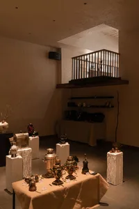 A cluttered interior space with vases and bottles scattered around, dimly lit creating a moody ambiance
