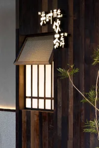 A traditional Asian building with wooden walls and a sliding door, surrounded by two potted plants with green leaves, featuring a window with a screen