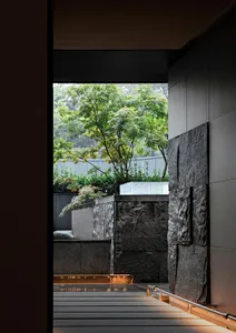 A calm bathroom space with a stone wall, a window for natural light, and two potted plants near the sink