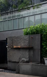 A modern building with a stone wall and metal pipe, surrounded by potted plants, conveying a sense of functionality and design