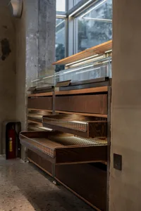 A restaurant interior with a wooden counter and glass display case featuring organized shelves with bottles and cups