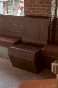 A room with a wooden bench and brick wall, featuring a brown leather seat and natural light from a window