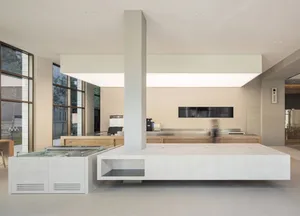 Open kitchen with a large island featuring a sink and refrigerator, two ovens, and white cabinets and walls