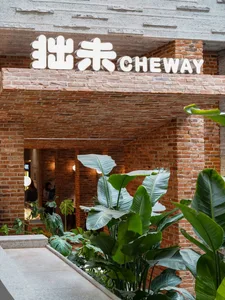 A cozy restaurant with a brick wall, potted plants, and natural lighting, featuring two people in the space