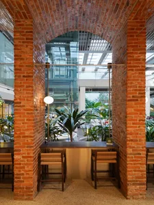 A well-lit interior space with a brick wall, glass ceiling, potted plants, and multiple chairs in various positions