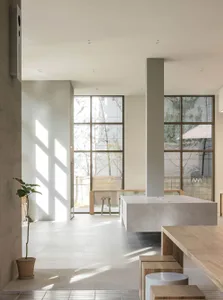 Open living area with concrete floor, white walls, natural light, a couch, dining table, chairs, and a potted plant