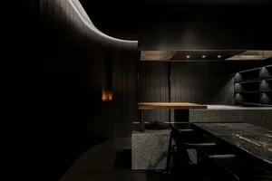 Industrial kitchen with a large stove top oven, black walls and floors, and a dining table with chairs