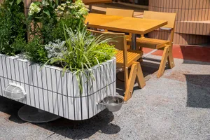 Outdoor dining area with two tables and chairs, surrounded by a potted plant and natural surroundings