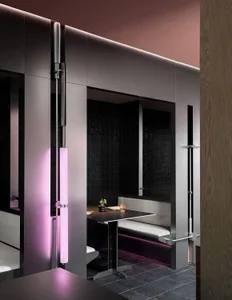 A modern bathroom with two sinks, two toilets, a black countertop, and a pink light above, with a vase on the countertop
