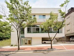 A modern building with a large glass window, surrounded by a parking area with two cars, under natural daylight