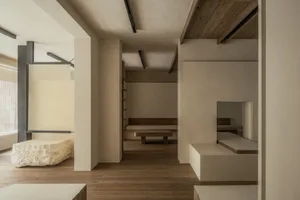 A calm and inviting empty room with wooden floors and white walls, featuring two benches and a large open area