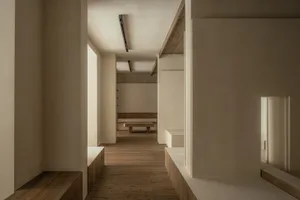 Empty white room with wooden floors and walls, featuring two benches and a calm atmosphere