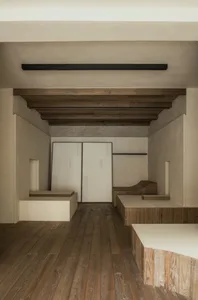 Empty room with wooden floors and walls, featuring two benches and a chair, creating a calm and inviting atmosphere