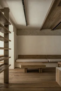 Empty living space with wooden floors and walls, featuring two benches, a dining table, and chairs in a minimalist and clean atmosphere