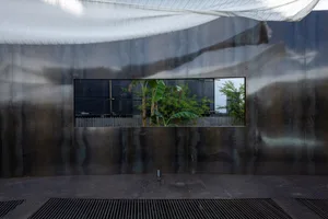 Industrial building with a metal wall and a window, surrounded by two banana trees