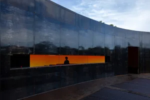 A person stands in front of a window with orange light, in a modern building with a black facade