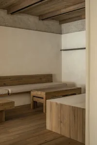 Small room with wooden floors, white walls, two beds with benches, and a dining table, creating a cozy and functional space
