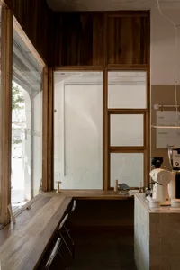 A warm and inviting coffee shop interior with a counter, cappuccino machine, sink, chairs, and a dining table in the background