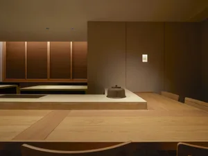 Empty kitchen with wooden floors and walls, featuring two dining tables and a chair, with a calm and inviting atmosphere