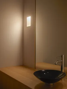 A clean bathroom with a sink on the right, a mirror above it, and two lights, one near the left edge and one near the center, creating a well-lit and inviting atmosphere