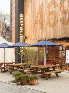 An outdoor dining area with wooden tables and chairs, umbrellas, and potted plants, creating a comfortable and inviting atmosphere