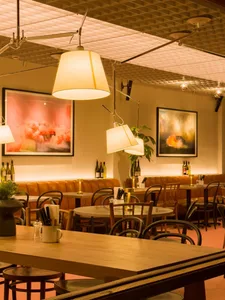 Dimly lit restaurant interior with a bar counter and chairs, surrounded by dining tables and bottles