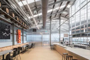 Industrial open space with a dining table and chairs, surrounded by a bar, with natural light coming in through windows or skylights