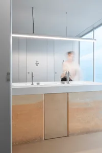 Modern bathroom with two sinks under a large window, two toilets, and ample space for users, with natural light entering the room