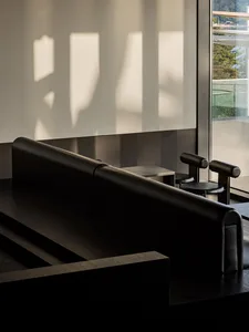 Comfortable living space with two black couches, three chairs, and natural light from a window