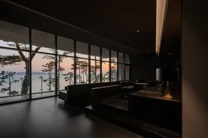 Luxurious living area with a black theme, featuring a large window with a water view, chairs, and a dining table