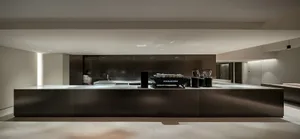 Modern kitchen with black countertops and cabinets, featuring two sinks, a coffee maker, and an oven, with cups scattered around the space