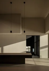 A modern dining space with a concrete wall, a dining table, chairs, and a couch, lit by natural light from a window