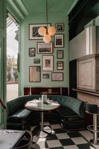 A modern dining space with a green table surrounded by chairs, multiple pictures on the wall, and a couch, creating a well-lit and inviting atmosphere