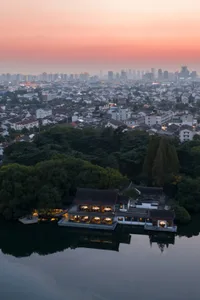 A cityscape at dusk with a large building featuring a distinctive red roof, surrounded by modern and historical architecture