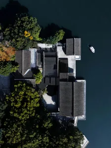 Asian-style house near a body of water with a black roof, surrounded by trees and a boat docked nearby