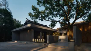Asian-style building with a gray concrete exterior, surrounded by two trees and natural foliage