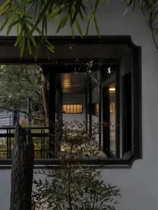 Asian-style house with a large window, black door, white wall, potted plants, and a bench in a well-lit room