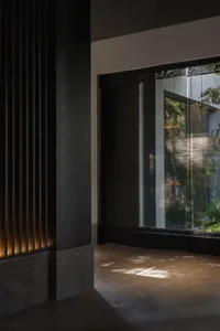 Dimly lit interior space with a black doorway, window with blinds, and potted plants on either side