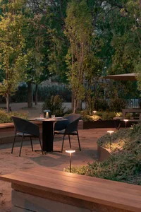 A relaxed outdoor dining area with a wicker table and chairs, surrounded by lush greenery and natural light