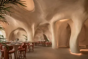 A modern restaurant interior with multiple tables and chairs, potted plants, and a welcoming atmosphere