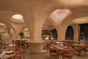 Modern restaurant interior with curved walls, potted plants, and a large dining area with multiple tables and chairs