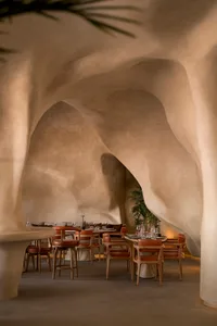 A well-lit dining area with multiple tables and chairs, wine glasses, and potted plants, creating an elegant and inviting atmosphere