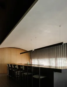 Modern kitchen with a central island featuring a black countertop, surrounded by chairs and bottles