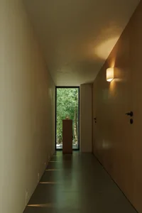 Narrow interior hallway with a wooden door and a glass door, painted white walls, and a focus on functionality