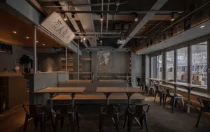 Empty industrial restaurant interior with a large dining table and multiple chairs, a couch in the background, and a commercial atmosphere