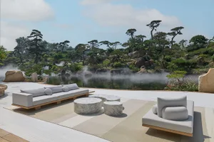 A relaxing living area with a wooden deck, a large couch, two chairs, and three round tables, overlooking a body of water
