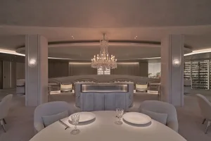 A formal dining space with a long table, chairs, and marble surfaces, set with plates and wine glasses, in a well-lit room with high ceilings and tasteful decorations