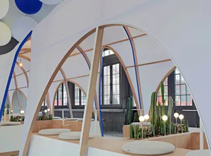 Modern cafe with a white dome structure, wooden accents, potted plants, and cacti, creating a clean and inviting atmosphere for seating and socializing