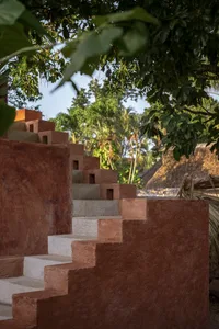 A rustic stone staircase leads up to a building surrounded by palm trees in a tranquil tropical environment