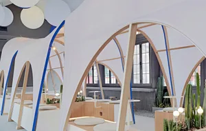 A modern cafe with a white canopy structure, wooden elements, and potted plants, creating a comfortable and inviting atmosphere for socializing and dining